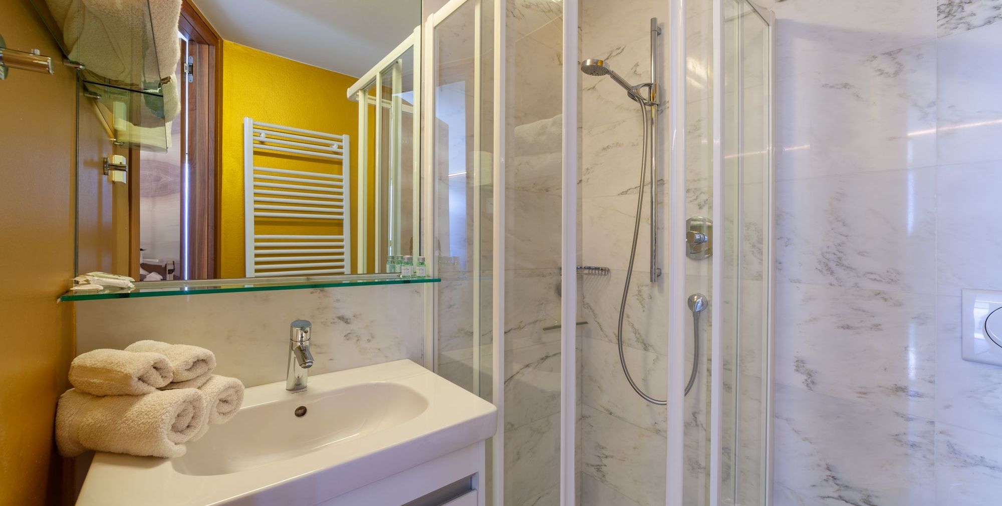 Modernes kleines Badezimmer mit Waschbecken, gefalteten Handtüchern und Glastür-Dusche.