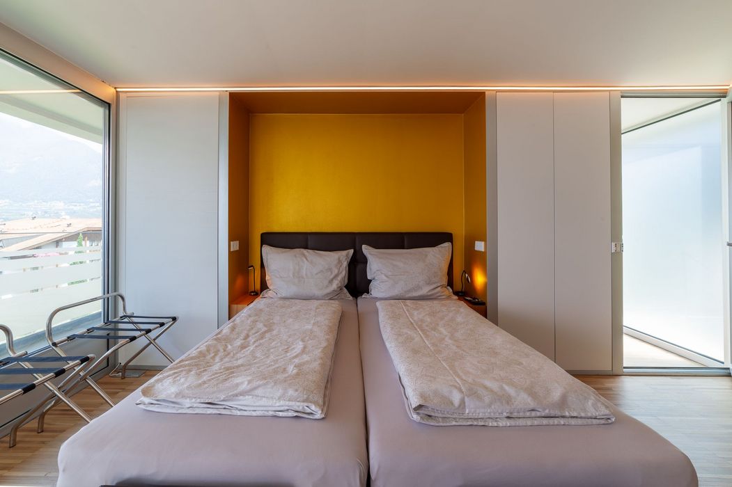 Schlafzimmer mit zwei Einzelbetten vor gelber Nische und großem Fenster
