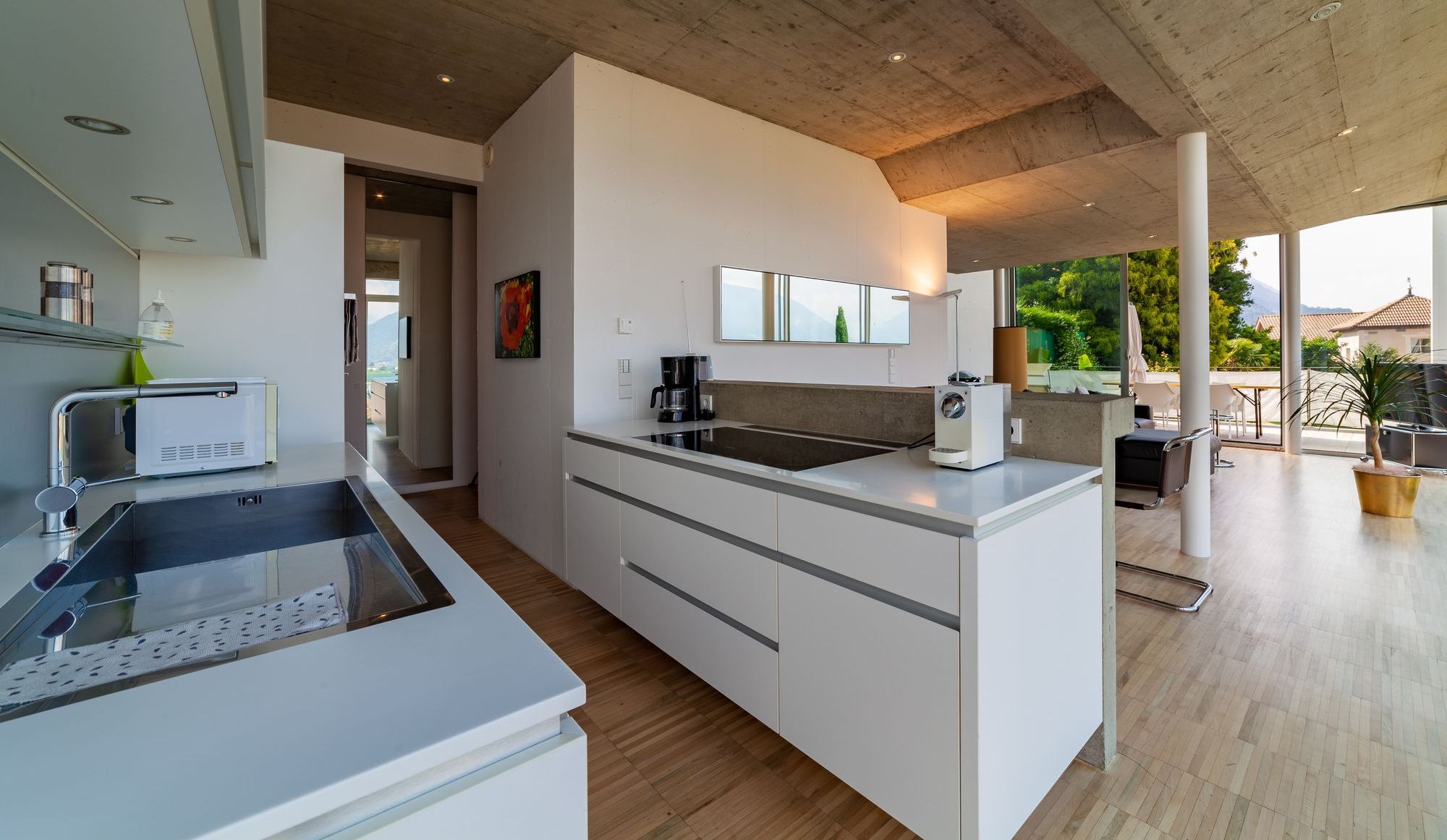 Helle, moderne offene Küche mit Kücheninsel, Sichtbetondecke und großen Fensterfronten zur Terrasse