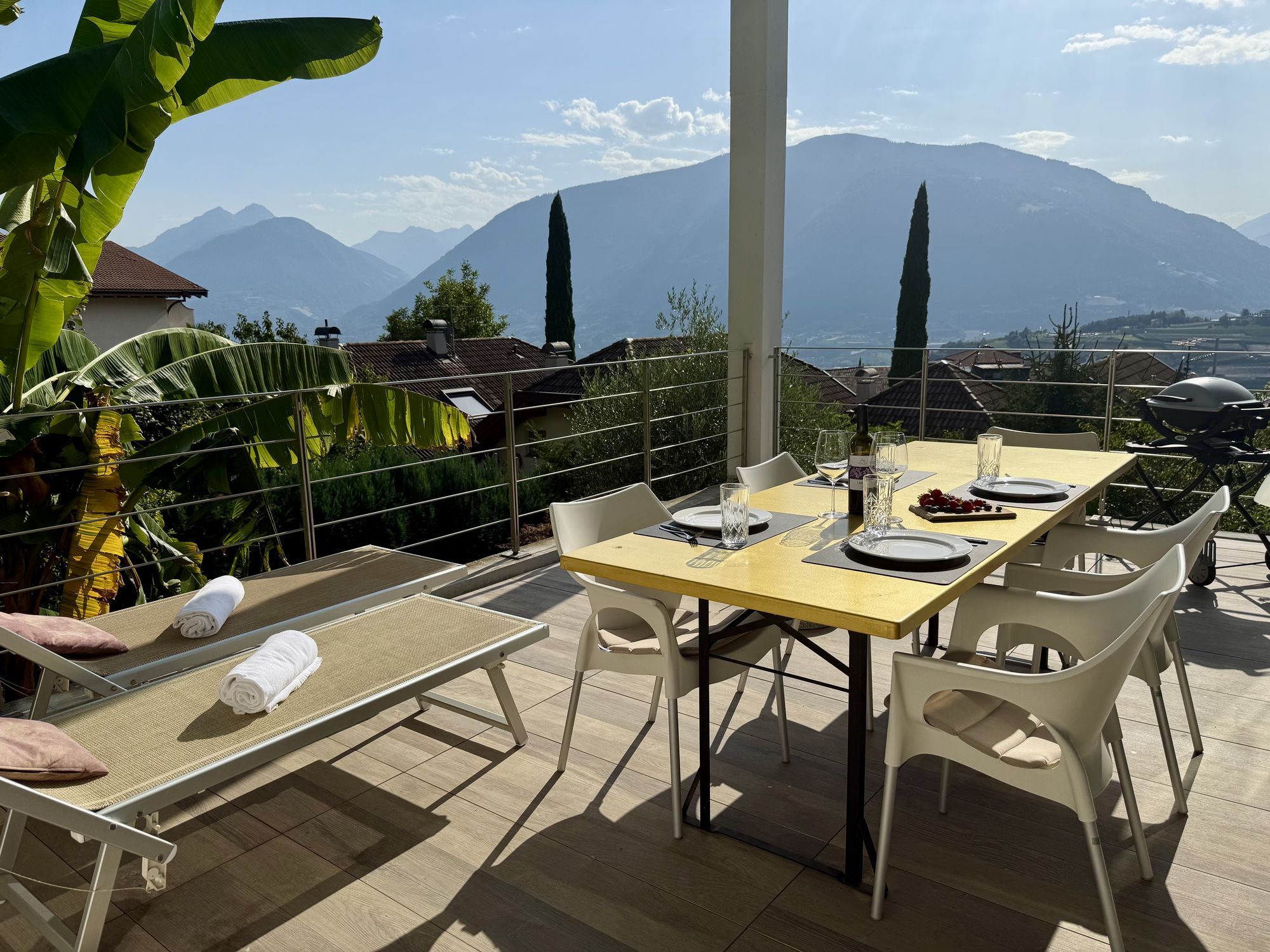 Terrasse mit gelbem Esstisch, gedeckten Plätzen, Liegestühlen und Bergpanorama