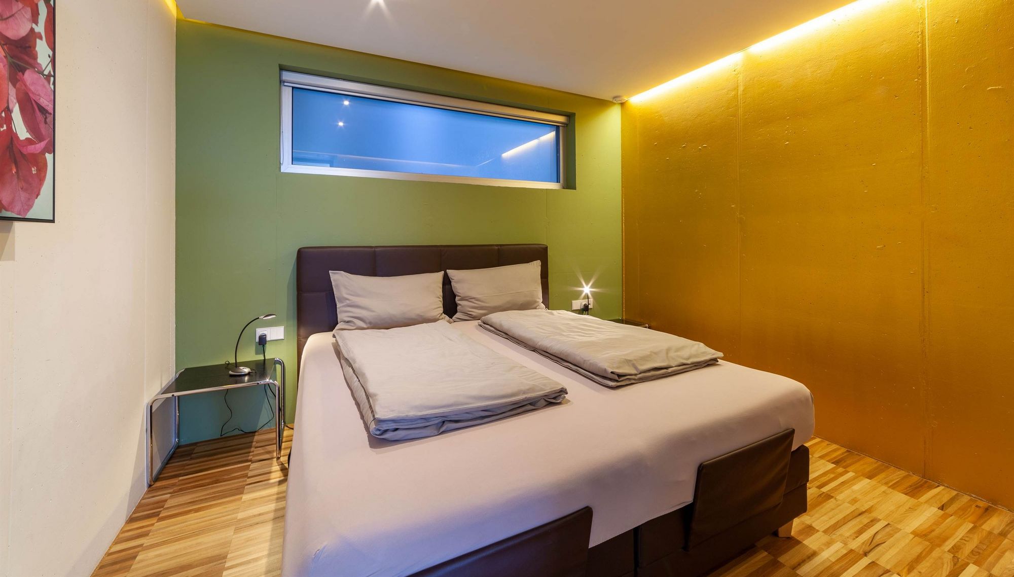 Modernes Schlafzimmer mit Doppelbett, grüner und gelber Wand sowie schmalem Fenster