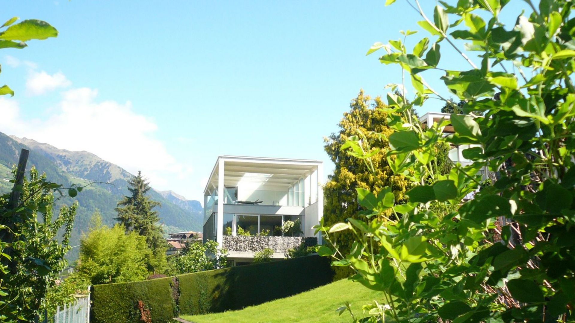 Casa moderna con ampie vetrate in un giardino verde, montagne sullo sfondo