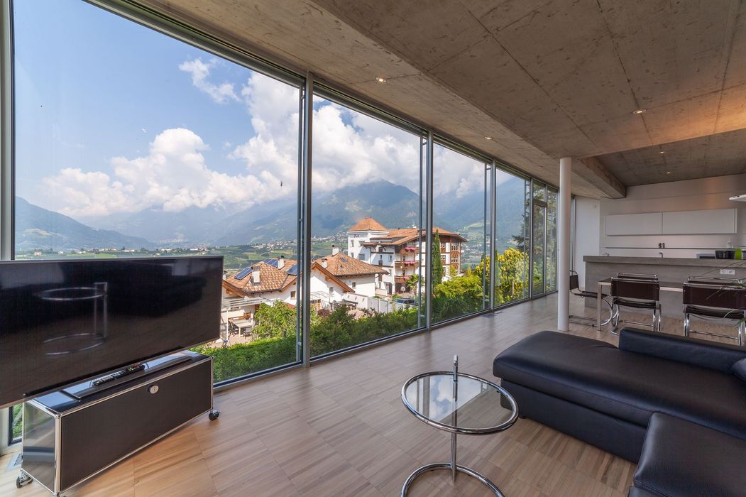 Modernes Wohnzimmer mit bodentiefen Fenstern, Blick auf Dächer und Berge, Couch und Fernseher