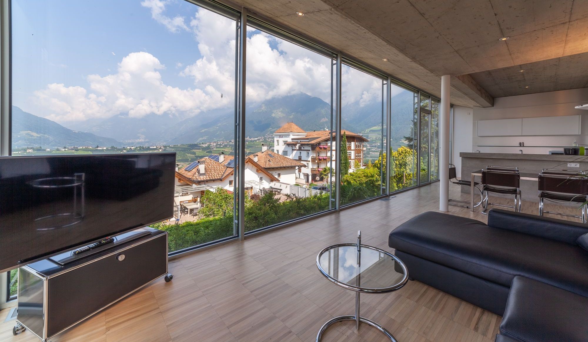 Modernes Wohnzimmer mit bodentiefen Fenstern, Blick auf Dächer und Berge, Couch und Fernseher