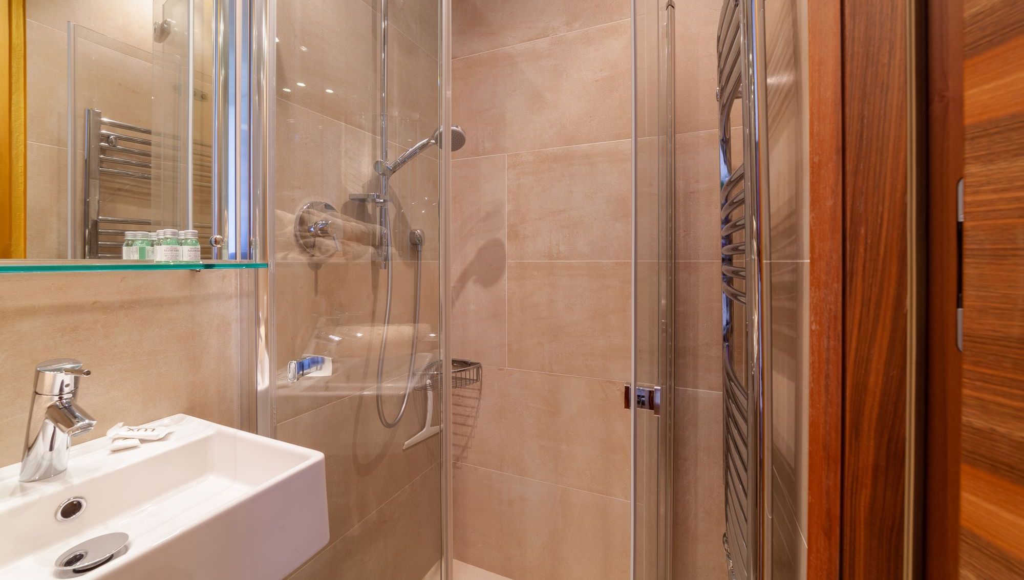 Kleines modernes Badezimmer mit Glasdusche, beigen Fliesen, Handbrause und Waschbecken.