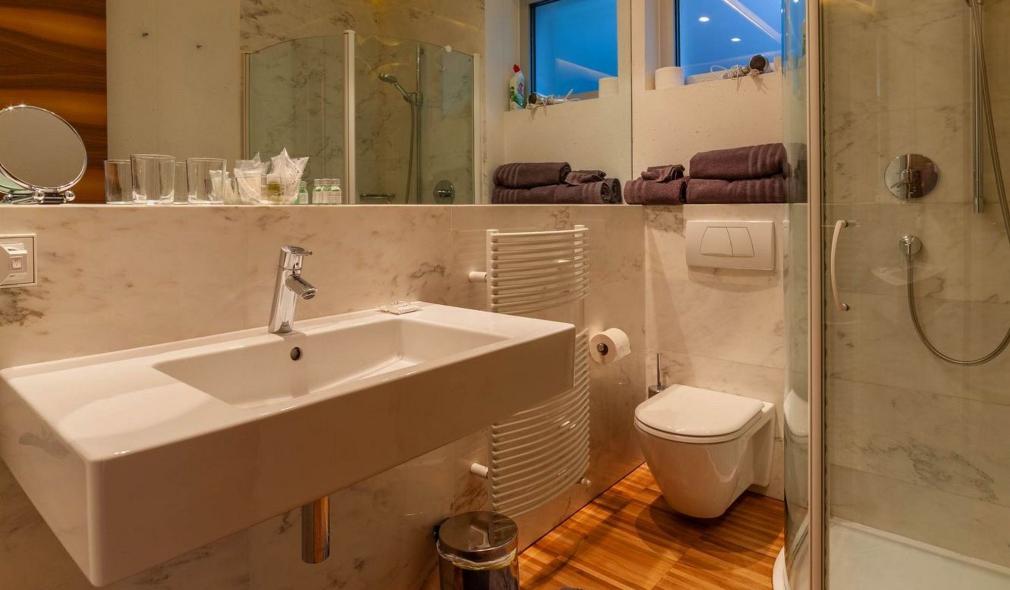 Modernes Badezimmer mit Waschbecken, Glasdusche, Toilette und beleuchtetem Spiegel