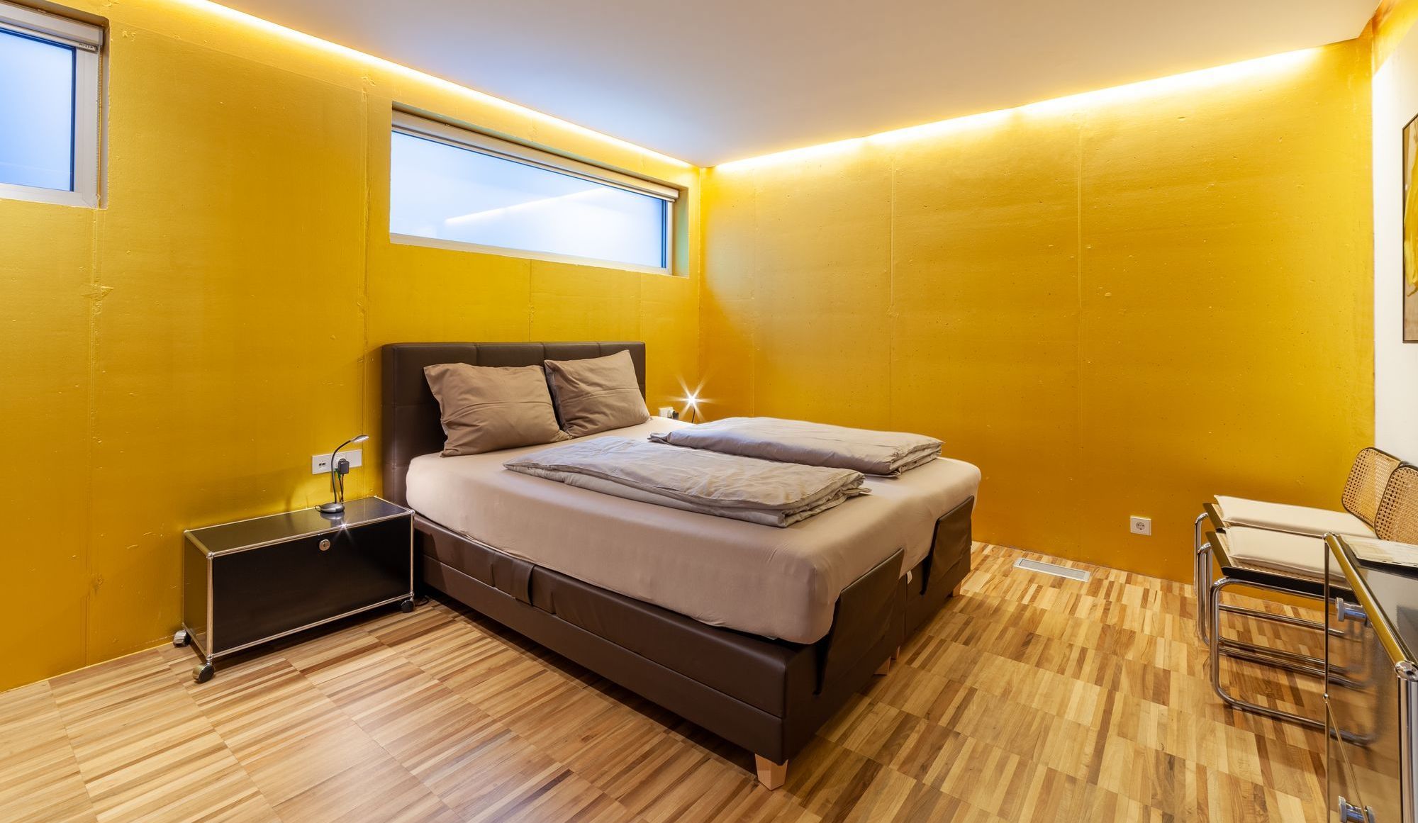 Modernes Schlafzimmer mit gelben Wänden, Doppelbett und Holzfußboden.