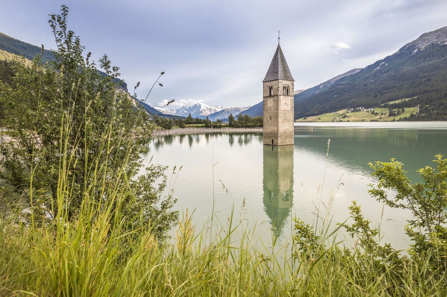 Versunkener Kirchturm in ruhigem Bergsee mit Bergen und Ufervegetation