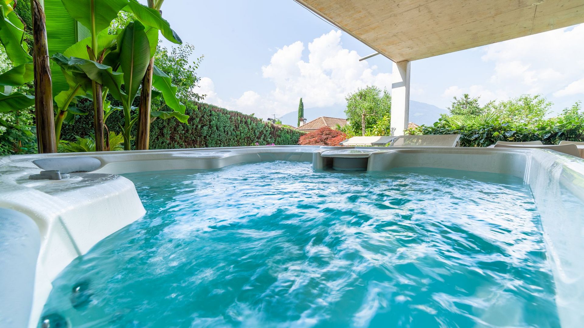 Idromassaggio all'aperto con acqua azzurra, piante tropicali e vista sul giardino.