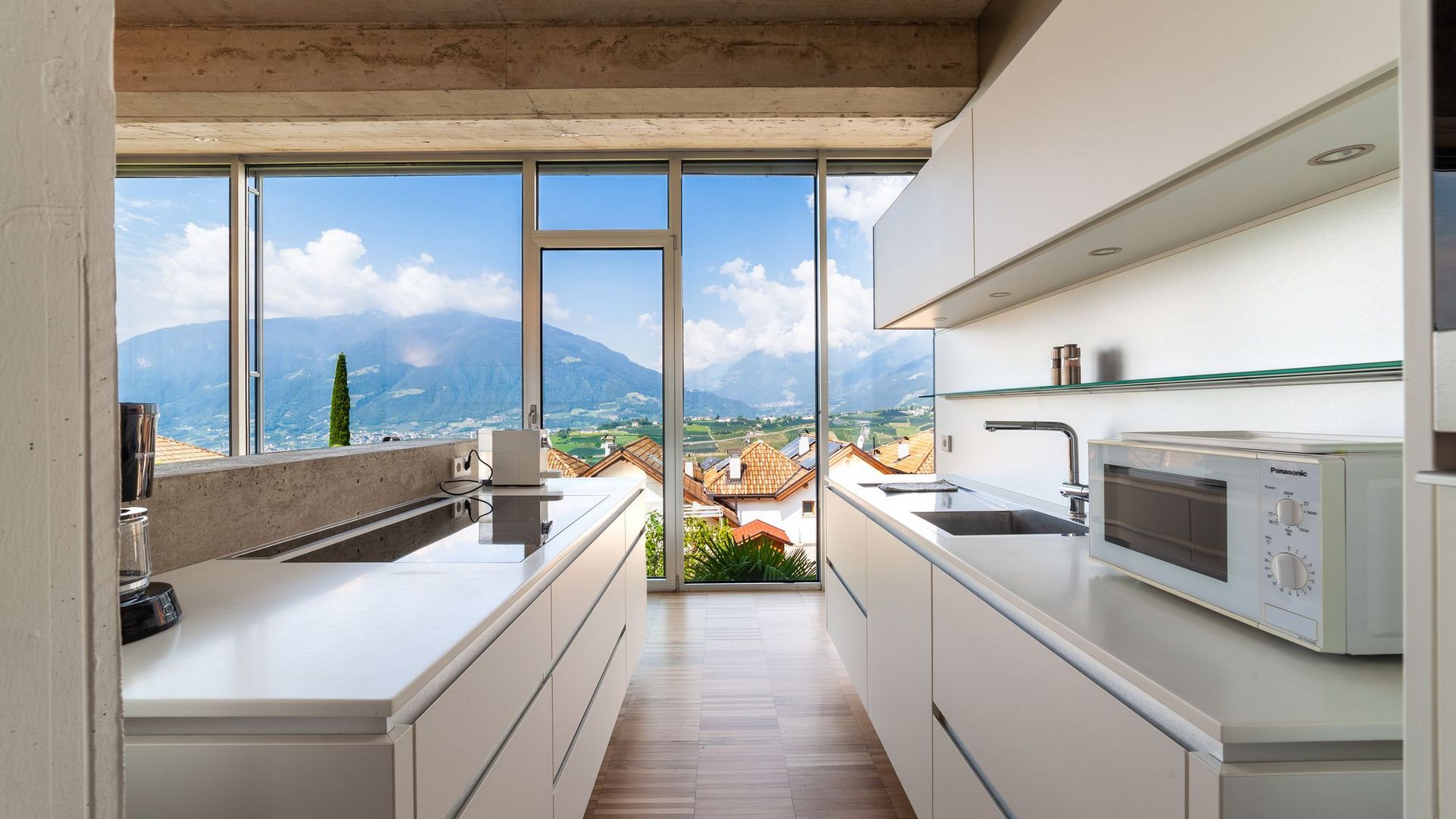 Cucina moderna bianca con grandi vetrate che si affacciano su tetti rossi e montagne al di là.