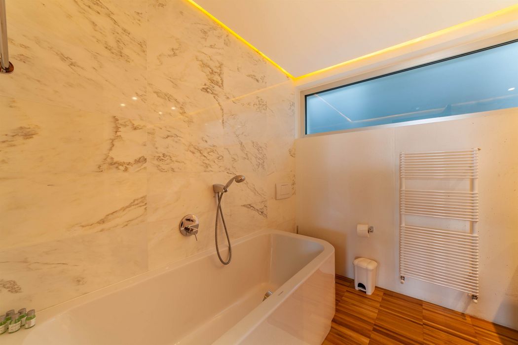 Modernes Badezimmer mit Wanne, Handbrause, Marmorfliesen und Handtuchheizung.