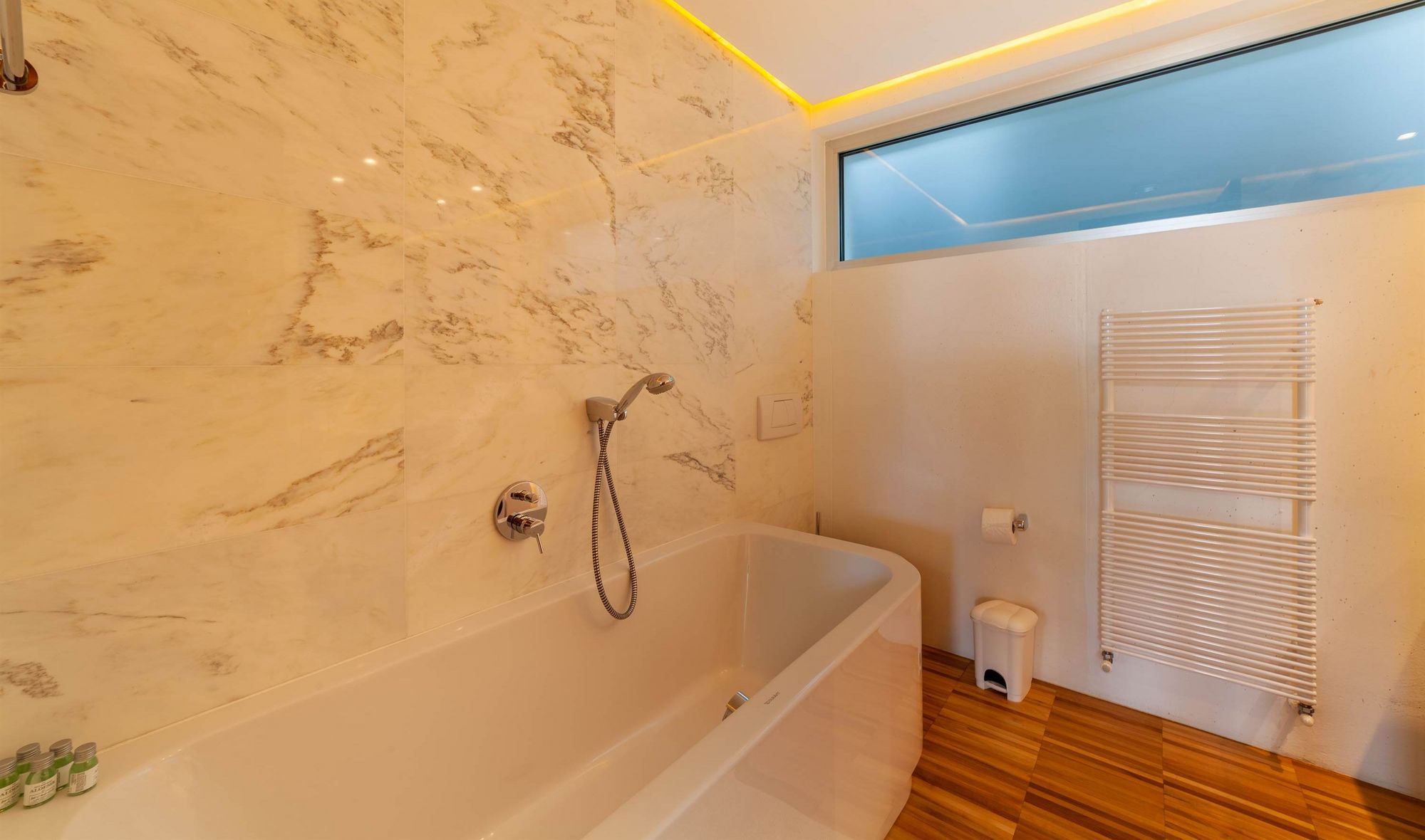 Modernes Badezimmer mit Wanne, Handbrause, Marmorfliesen und Handtuchheizung.