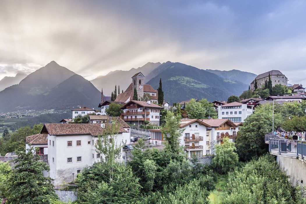Alpendorf mit Kirche, Schloss und Häusern vor Bergen im dunstigen Morgenlicht