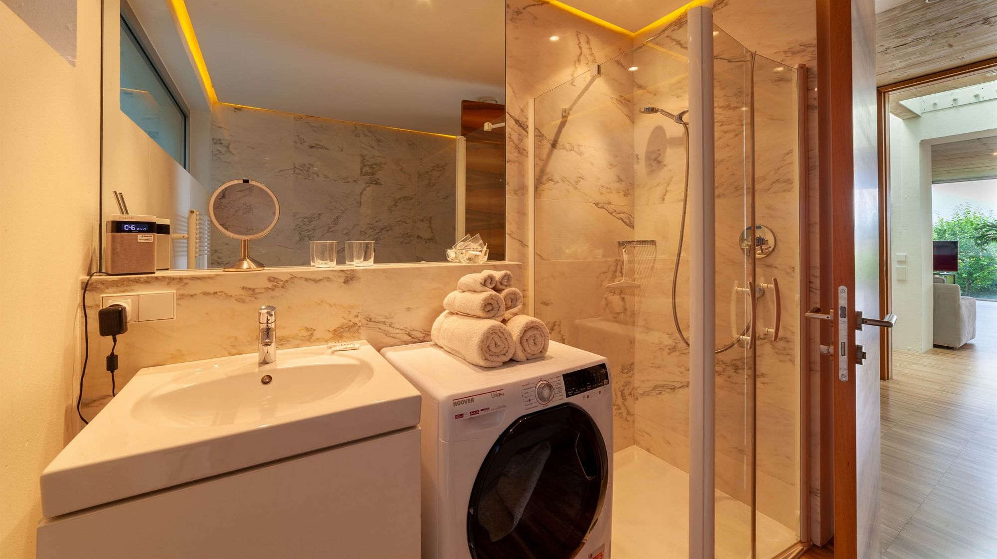 Modernes Badezimmer mit Waschbecken, Waschmaschine, gestapelten Handtüchern und Glastür zur Dusche.