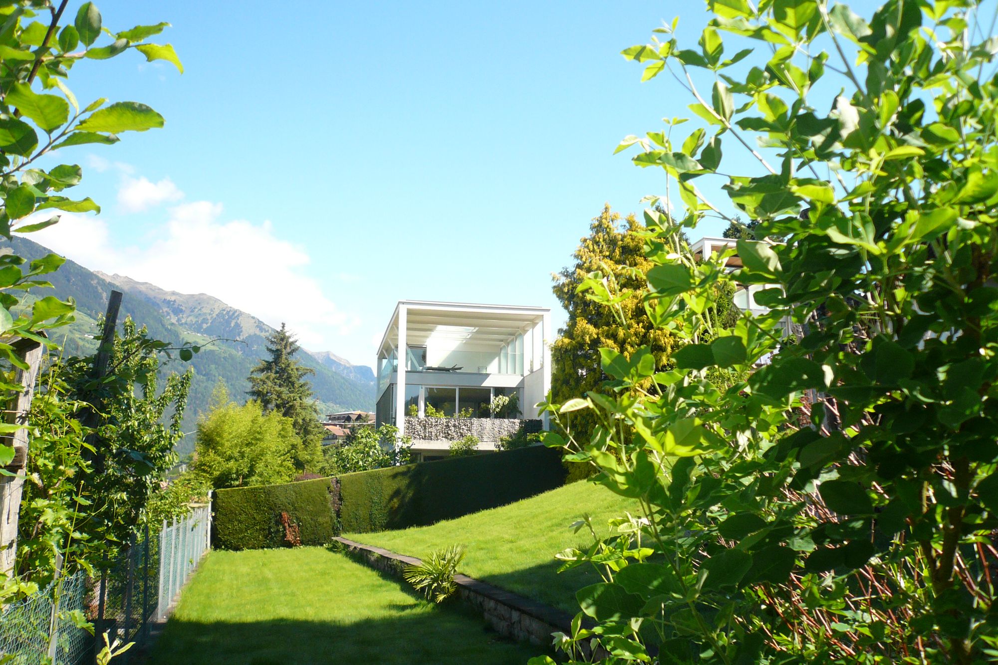 Casa moderna con ampie vetrate in un giardino verde, montagne sullo sfondo