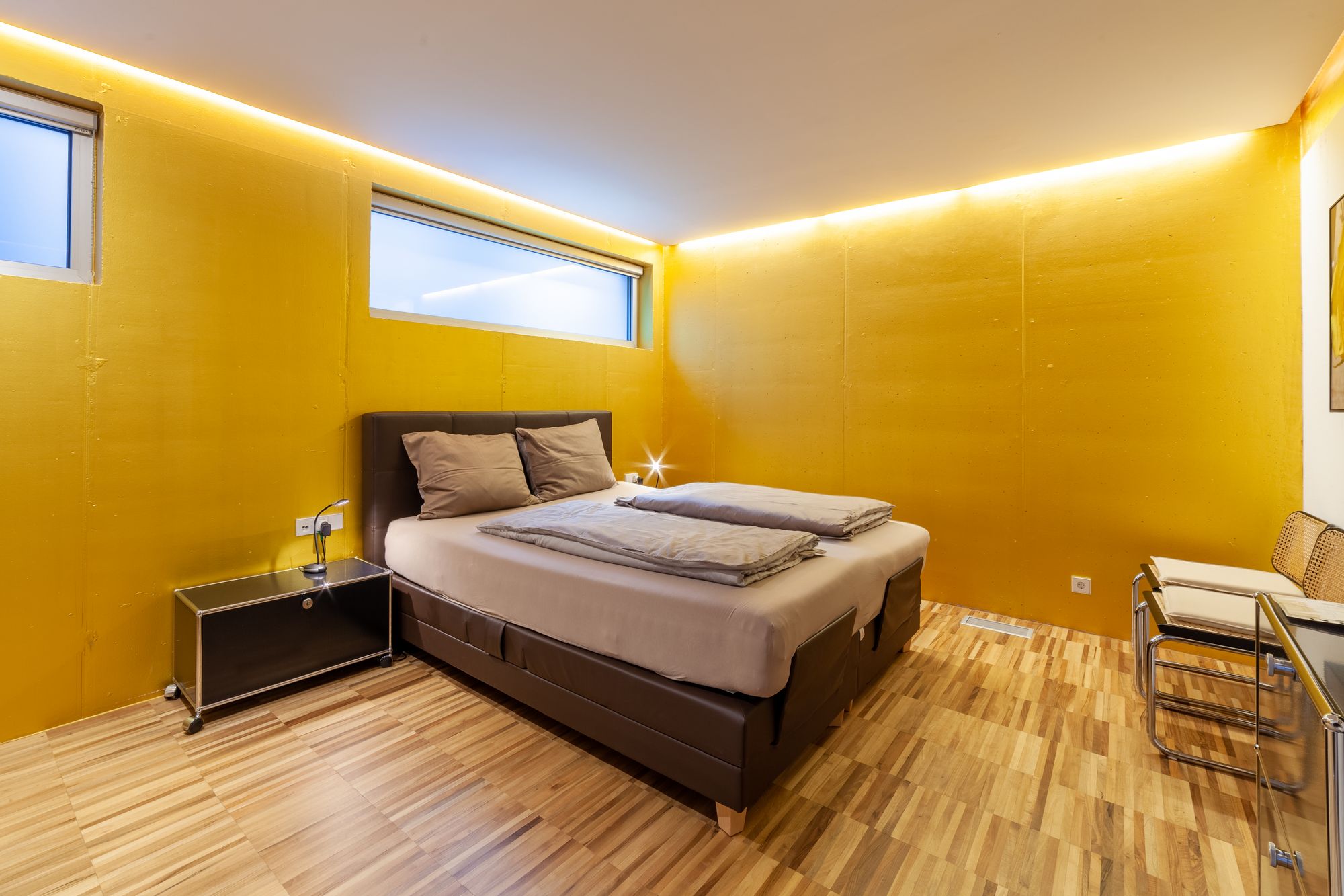 Camera da letto moderna con pareti gialle, letto matrimoniale beige, pavimento in legno e illuminazione a LED perimetrale.