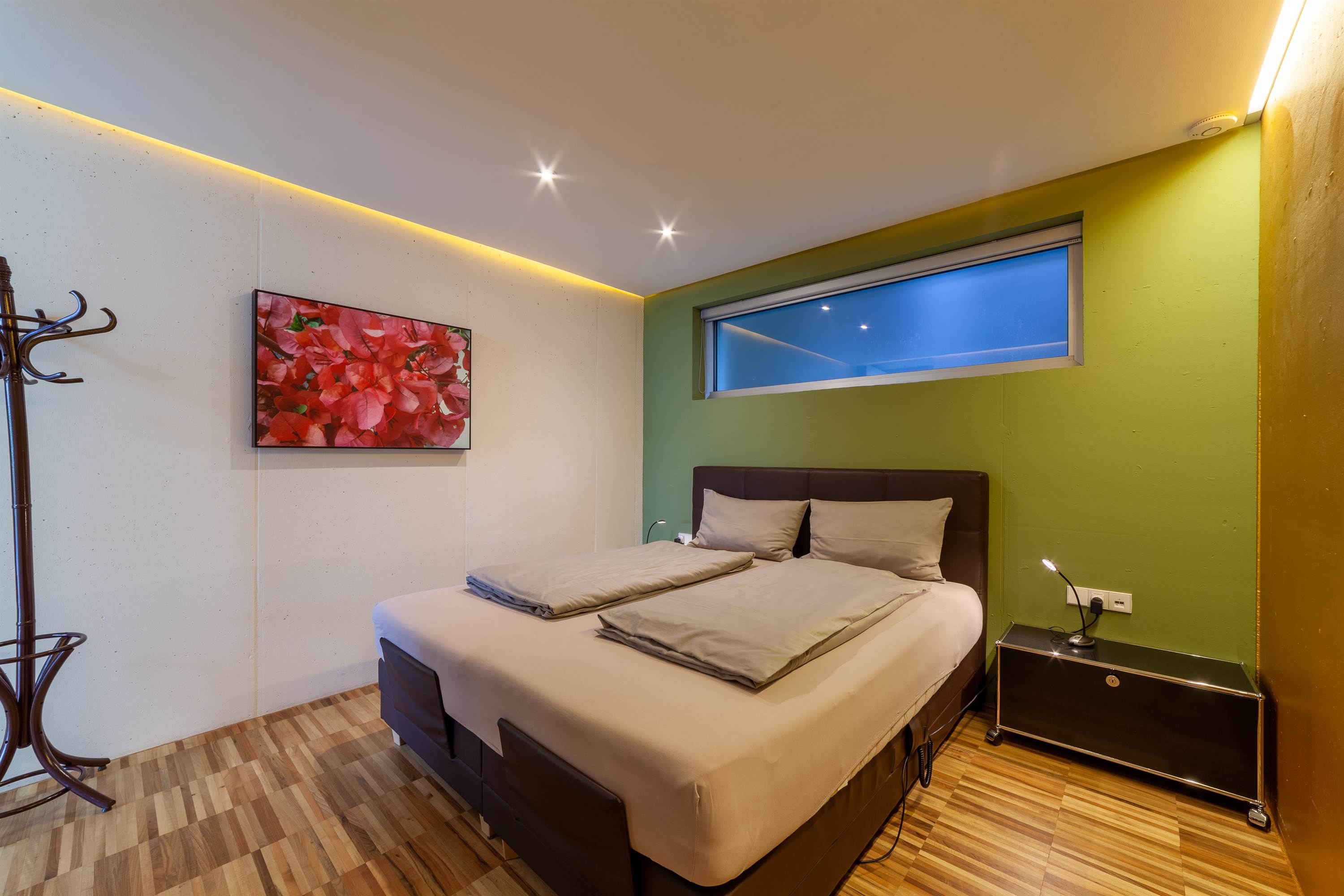 Camera da letto moderna con letto matrimoniale, parete verde, quadro di fiori rossi e illuminazione soffusa