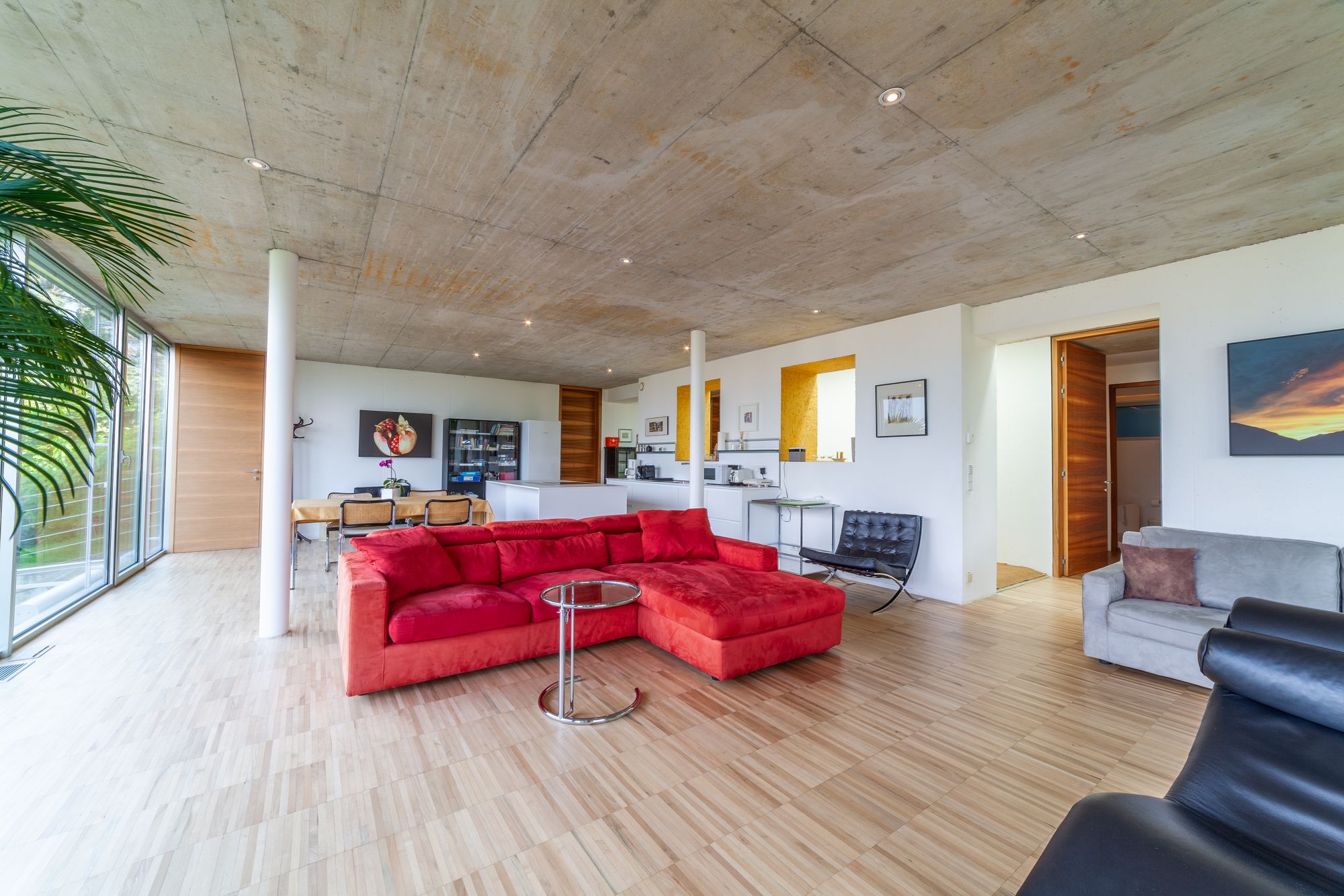 Soggiorno open-space moderno con soffitto in cemento, grande divano ad angolo rosso e ampie vetrate